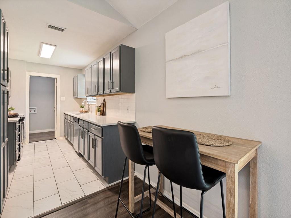 1405 Rambler Road Arlington, TX 76014 - Photo 10 of 26 Galley kitchen featuring white tile flooring, white subway tile backsplash, dark grey cabinetry, white countertops, and a wood-finish breakfast bar