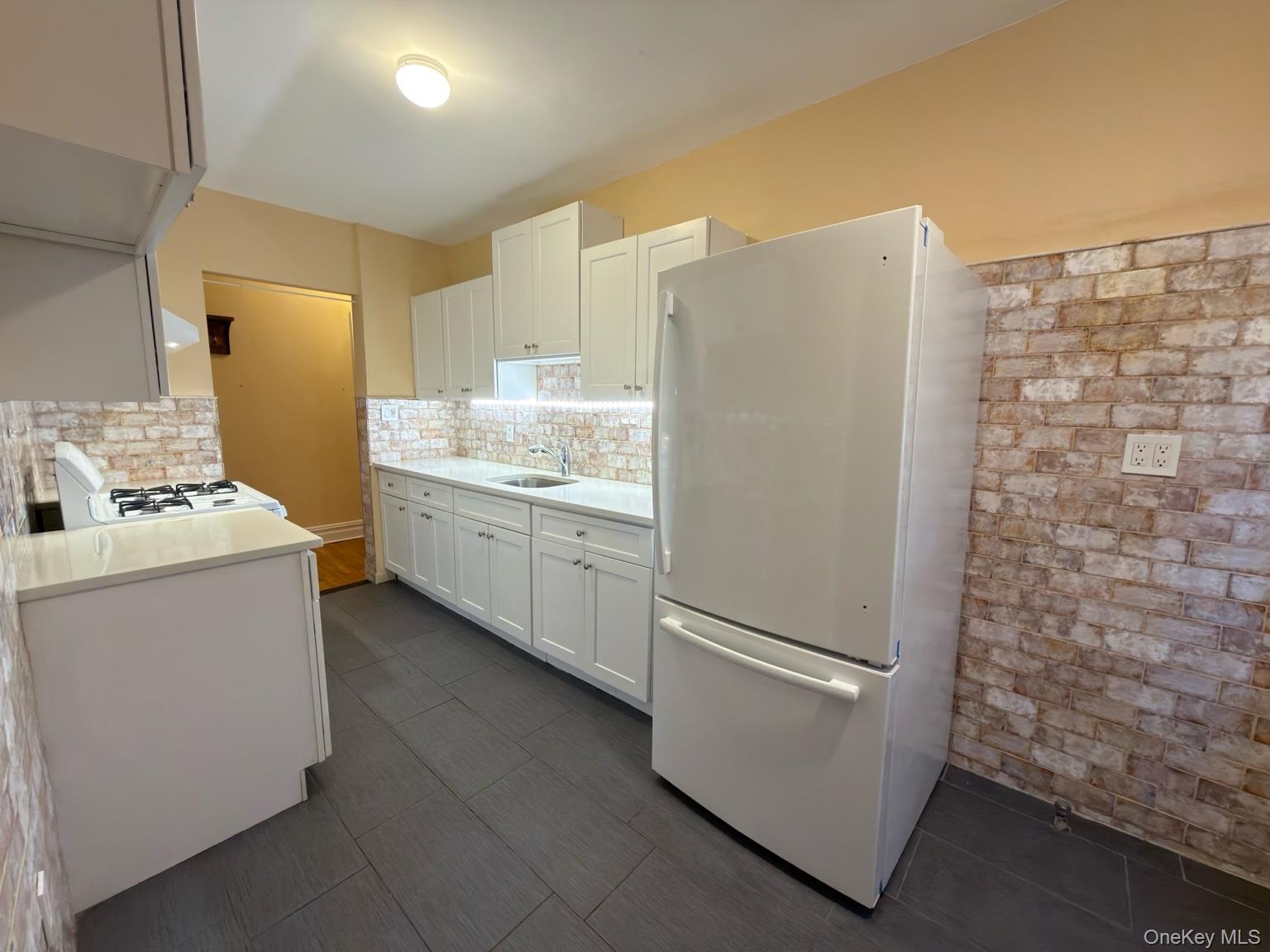 42 Barker Avenue, Unit 2B White Plains, NY 10601 - Photo 3 of 13 Kitchen featuring white appliances, white cabinets, brick wall, tasteful backsplash, and light stone countertops