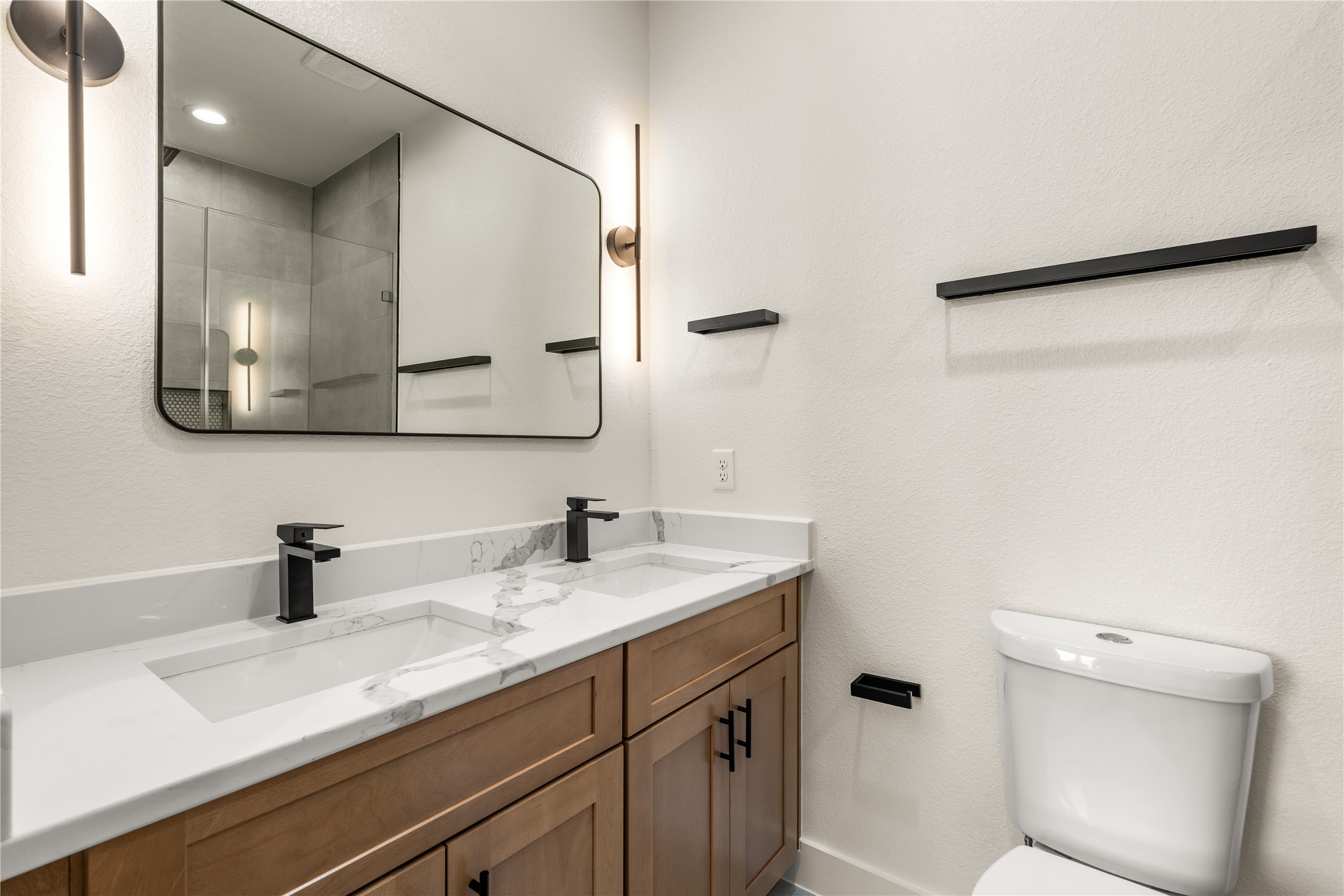 5321 Rue Street Houston, TX 77033 - Photo 14 of 23 Primary ensuite bath — quartz dual vanity, warm wood cabinetry, sleek matte black hardware, and designer sconce lighting.