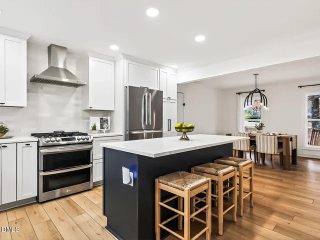 a kitchen with stainless steel appliances a dining table chairs stove refrigerator and cabinets