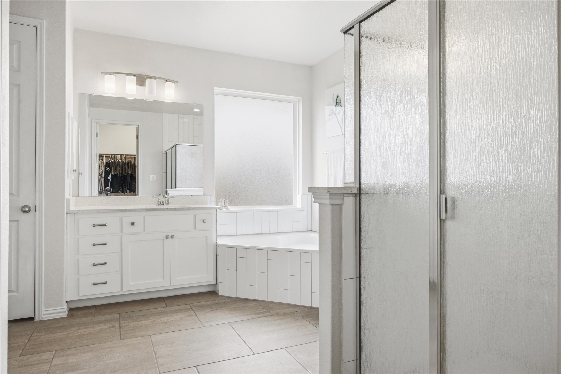 192 Raptor Beak Way Cedar Creek, TX 78612 - Photo 18 of 38 Bathroom featuring a glass-enclosed shower, corner soaking tub with white subway tile surround, single vanity with white cabinetry and light-toned countertop, and large format tile flooring