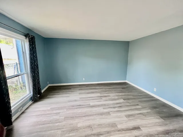 a view of an empty room with wooden floor and a window