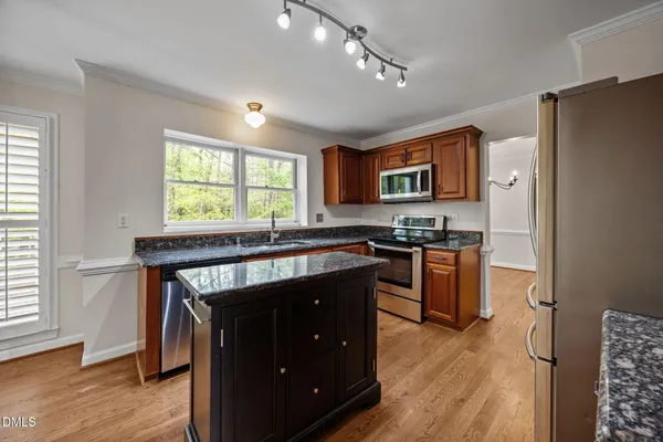 a kitchen with stainless steel appliances granite countertop wooden cabinets a refrigerator a stove a sink and dishwasher with wooden floor