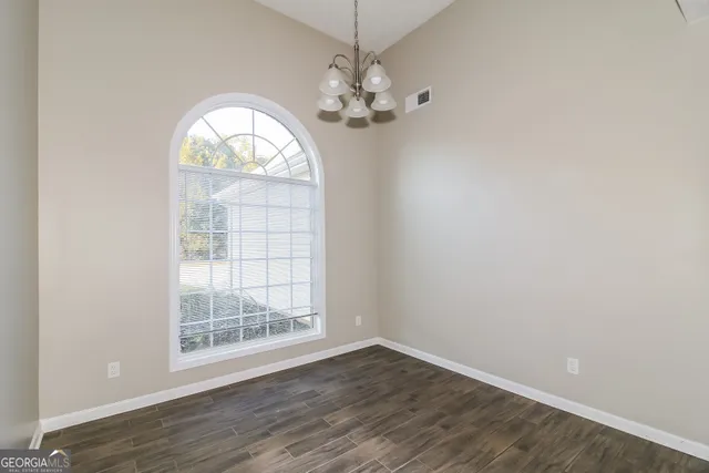 an empty room with wooden floor chandelier and windows