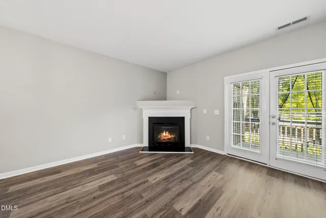 a view of an empty room with wooden floor fireplace and a window