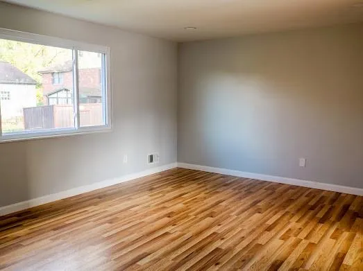 a view of an empty room with wooden floor and a window