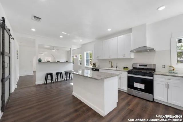 a kitchen with stainless steel appliances granite countertop a stove top oven a sink dishwasher and white cabinets with wooden floor