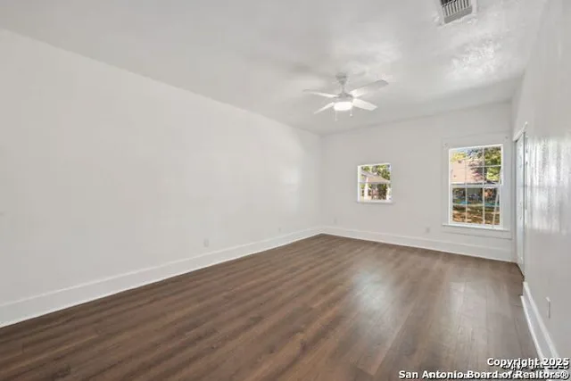 an empty room with wooden floor ceiling fan and windows