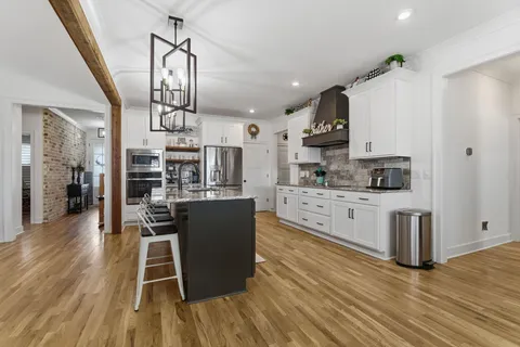 a kitchen with stainless steel appliances granite countertop a refrigerator a stove top oven a sink dishwasher and white cabinets with wooden floor