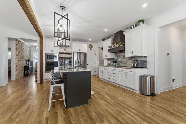 a kitchen with stainless steel appliances granite countertop a refrigerator a stove top oven a sink dishwasher and white cabinets with wooden floor