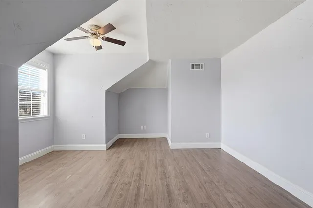 an empty room with wooden floor chandelier fan and windows