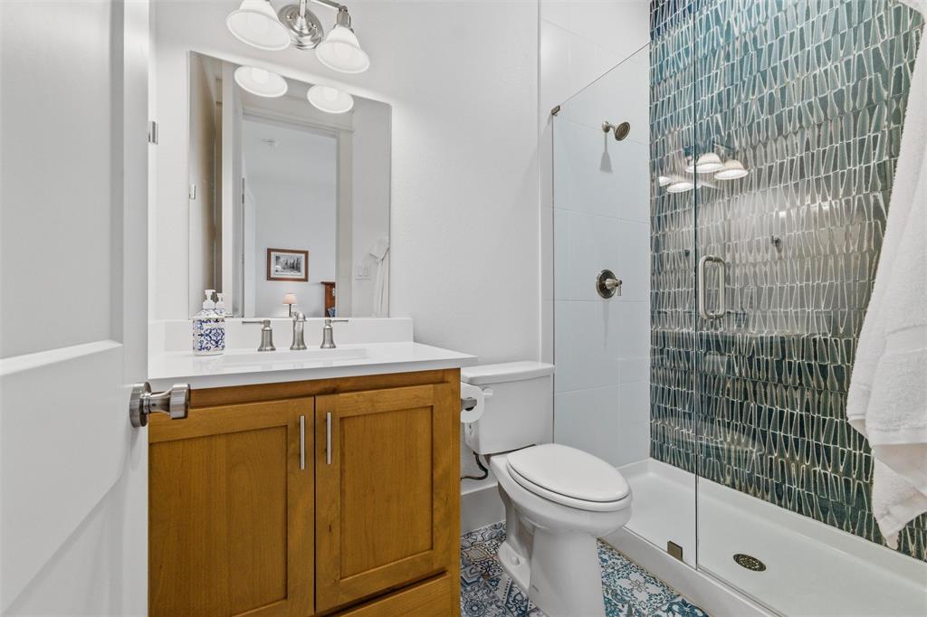 6625 Sandy Beach Road Azle, TX 76020 - Photo 19 of 40 Secondary bathroom features glass-enclosed walk-in shower with decorative full-height tile accent wall, wood-tone vanity cabinetry, quartz-style countertop, framed mirror, and patterned tile flooring throughout.