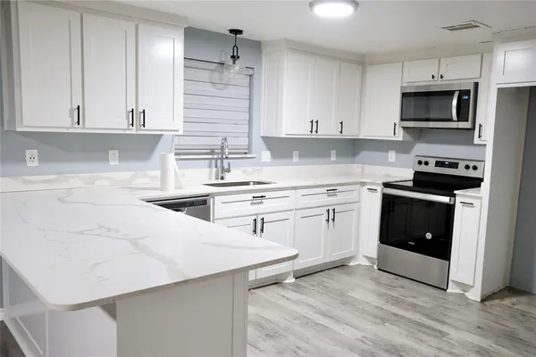 a kitchen with stainless steel appliances a stove top oven a sink a refrigerator and white cabinets