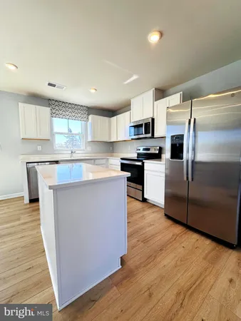 a kitchen with stainless steel appliances granite countertop a stove top oven a refrigerator and a granite counter tops with wooden floors