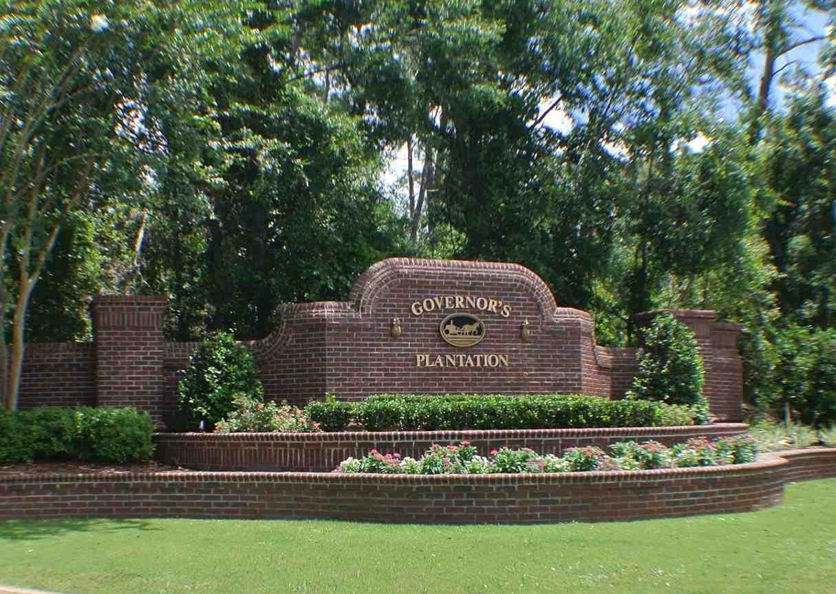 Community sign featuring a lawn and view of wooded area