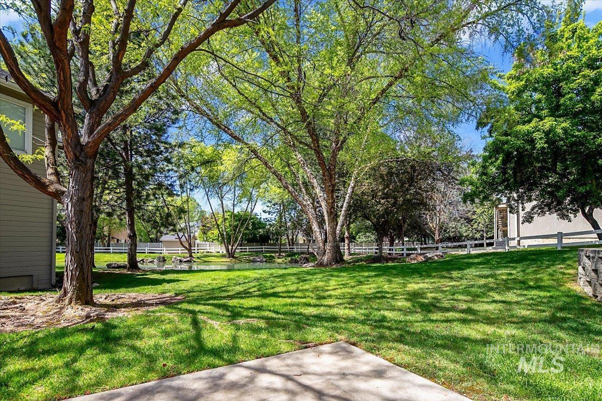 725 North Eagle Road Eagle, ID 83616 - Photo 38 of 45 Expansive green lawn with mature trees providing dappled shade, bordered by a white fence and a tranquil pond