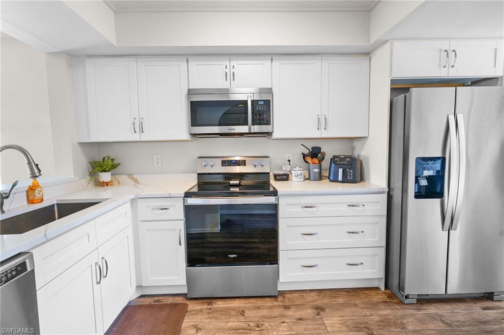 Kitchen featuring stainless steel appliances, white cabinetry, and light stone countertops