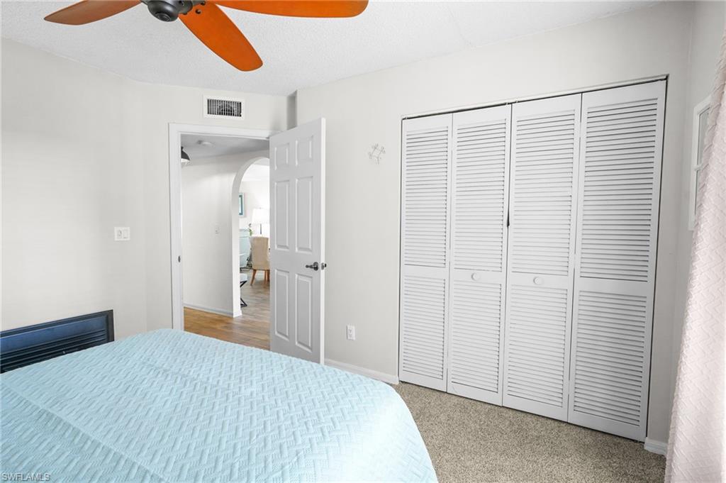 601 Augusta Boulevard, Unit 10 Naples, FL 34113 - Photo 15 of 27 Bedroom featuring arched walkways, a ceiling fan, light carpet, a closet, and a textured ceiling