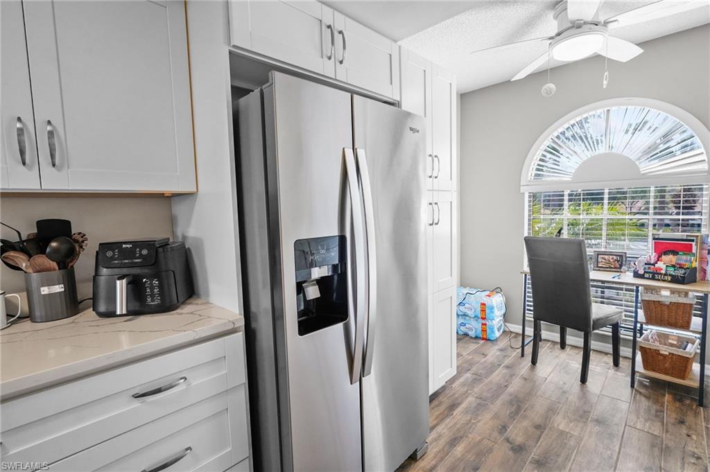 601 Augusta Boulevard, Unit 10 Naples, FL 34113 - Photo 9 of 27 Kitchen with stainless steel fridge with ice dispenser, white cabinetry, dark wood-type flooring, ceiling fan, and light stone countertops