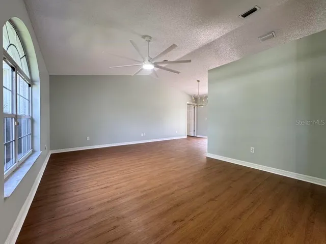 an empty room with wooden floor fan and windows