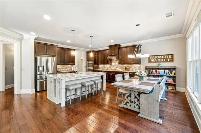 a kitchen with stainless steel appliances kitchen island granite countertop a table chairs and a refrigerator