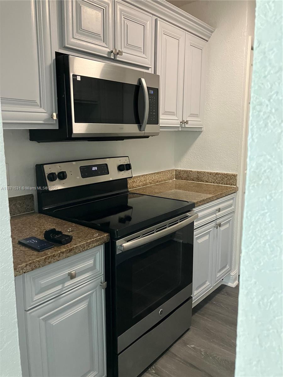 7256 Southwest 94th Place, Unit A1 Miami, FL 33173 - Photo 3 of 7 a kitchen with granite countertop white cabinets and stainless steel appliances