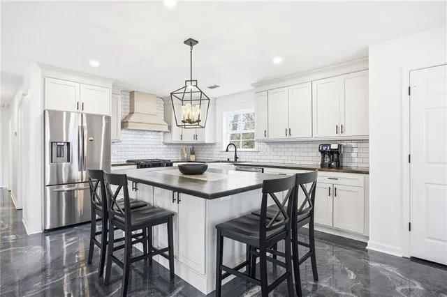 a kitchen with stainless steel appliances granite countertop a sink a stove a refrigerator and white cabinets with wooden floor