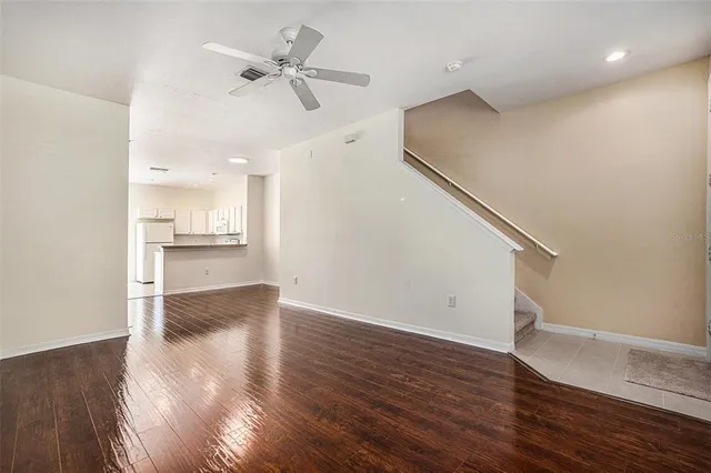 a view of an empty room with wooden floor and a ceiling fan