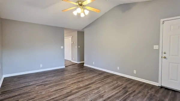 a view of an empty room with wooden floor and a chandelier fan