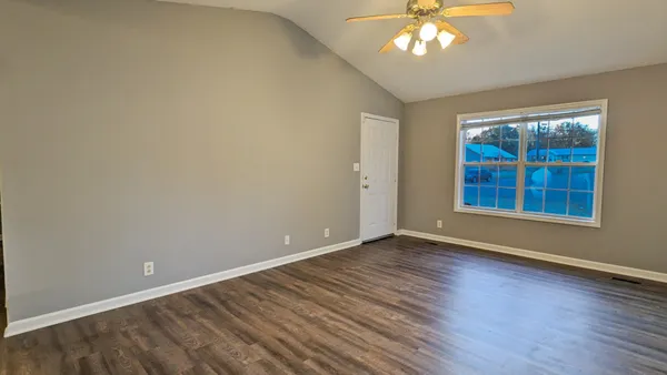 a view of an empty room with wooden floor and a window