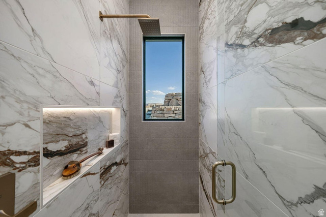 2867 East Granite Way St. George, UT 84790 - Photo 50 of 69 Shower featuring large format marble-look tile walls, a built-in recessed niche with accent lighting, and a rainfall showerhead with a gold-tone finish
