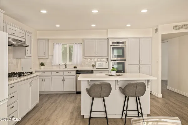 a kitchen with stainless steel appliances granite countertop a stove a sink and white cabinets with wooden floor