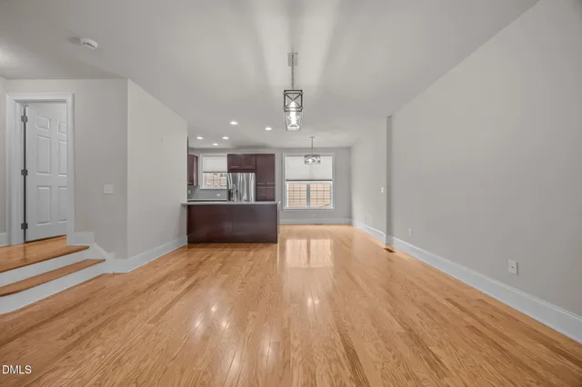 a view of empty room with wooden floor and kitchen