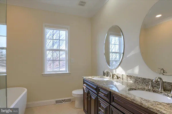 a bathroom with a granite countertop toilet a sink a mirror and a window