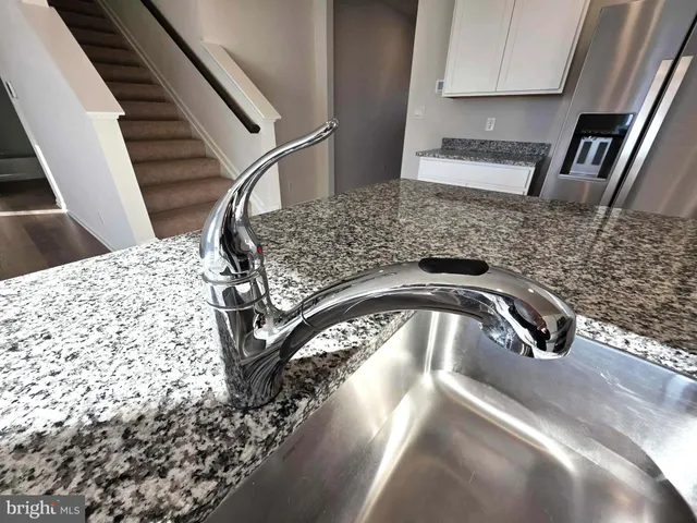 a kitchen with granite countertop a refrigerator a stove top oven a sink dishwasher and white cabinets with wooden floor