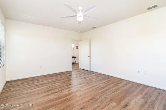 an empty room with wooden floor and a ceiling fan