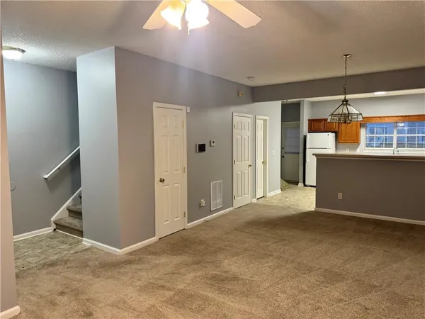 an empty room with kitchen view and a chandelier fan