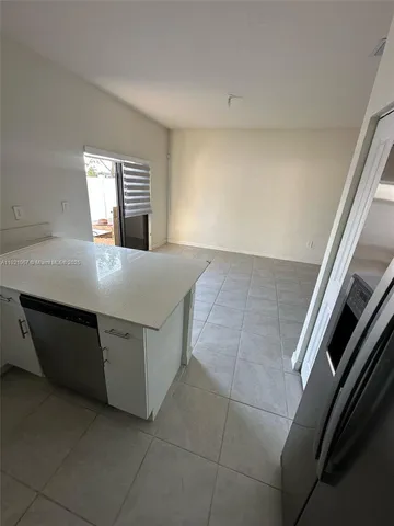 a view of an empty room with kitchen and window