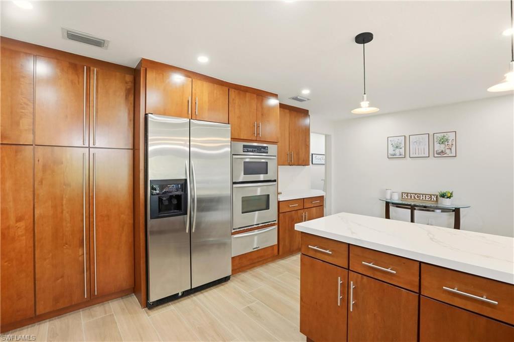 339 Landmark Street Marco Island, FL 34145 - Photo 16 of 50 Kitchen featuring brown cabinetry, appliances with stainless steel finishes, decorative light fixtures, light stone counters, and a warming drawer