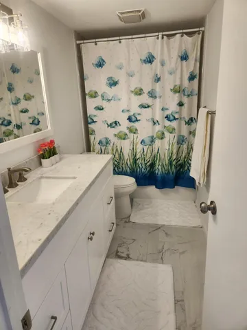 a bathroom with a granite countertop sink a toilet and shower curtain