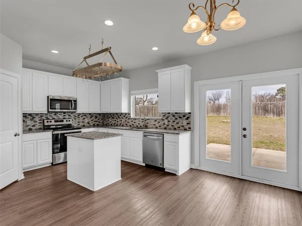 a kitchen with stainless steel appliances granite countertop a stove and white cabinets with wooden floor