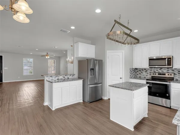 a kitchen with stainless steel appliances granite countertop a refrigerator a stove oven a sink dishwasher and white cabinets with wooden floor
