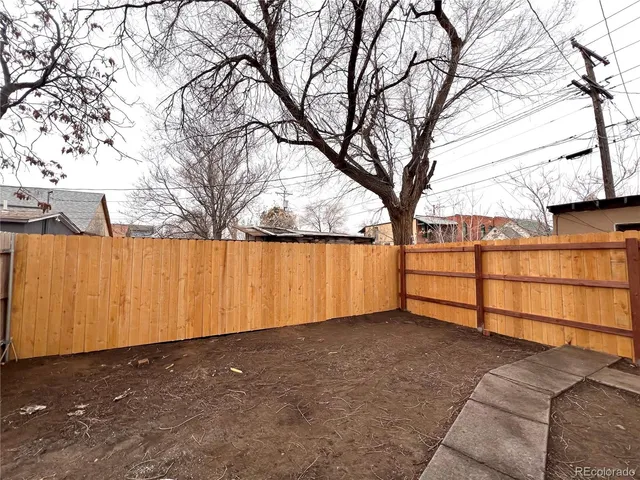 a backyard of a house with large trees and a wooden fence