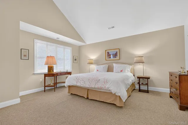 a spacious bedroom with a bed and a lamp on dresser