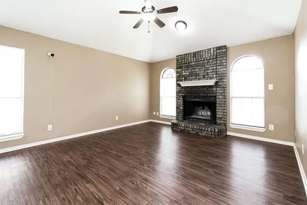 an empty room with wooden floor fireplace and windows