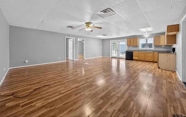 a view of an empty room with wooden floor and a kitchen