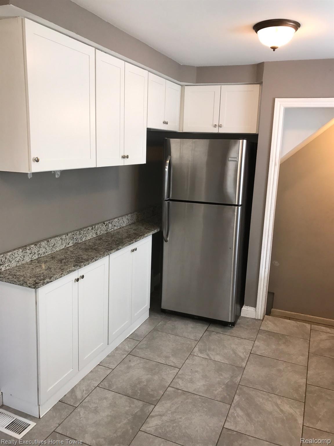 2427 Cambridge Road Berkley, MI 48072 - Photo 7 of 17 Kitchen area featuring white shaker-style cabinetry, a stainless steel refrigerator, speckled countertops, and tile flooring