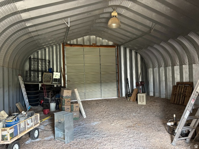 14908 North Deep Crk Road Lapoint, UT 84039 - Photo 8 of 9 Quonset-style metal building featuring a large roll-up door, corrugated metal interior walls, a gravel floor, and an overhead light fixture
