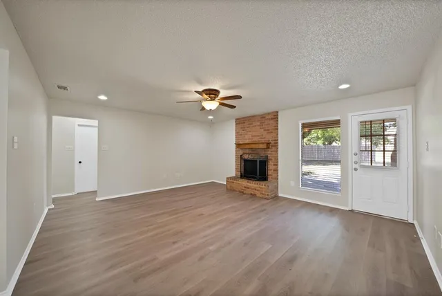 an empty room with wooden floor chandelier fan and windows