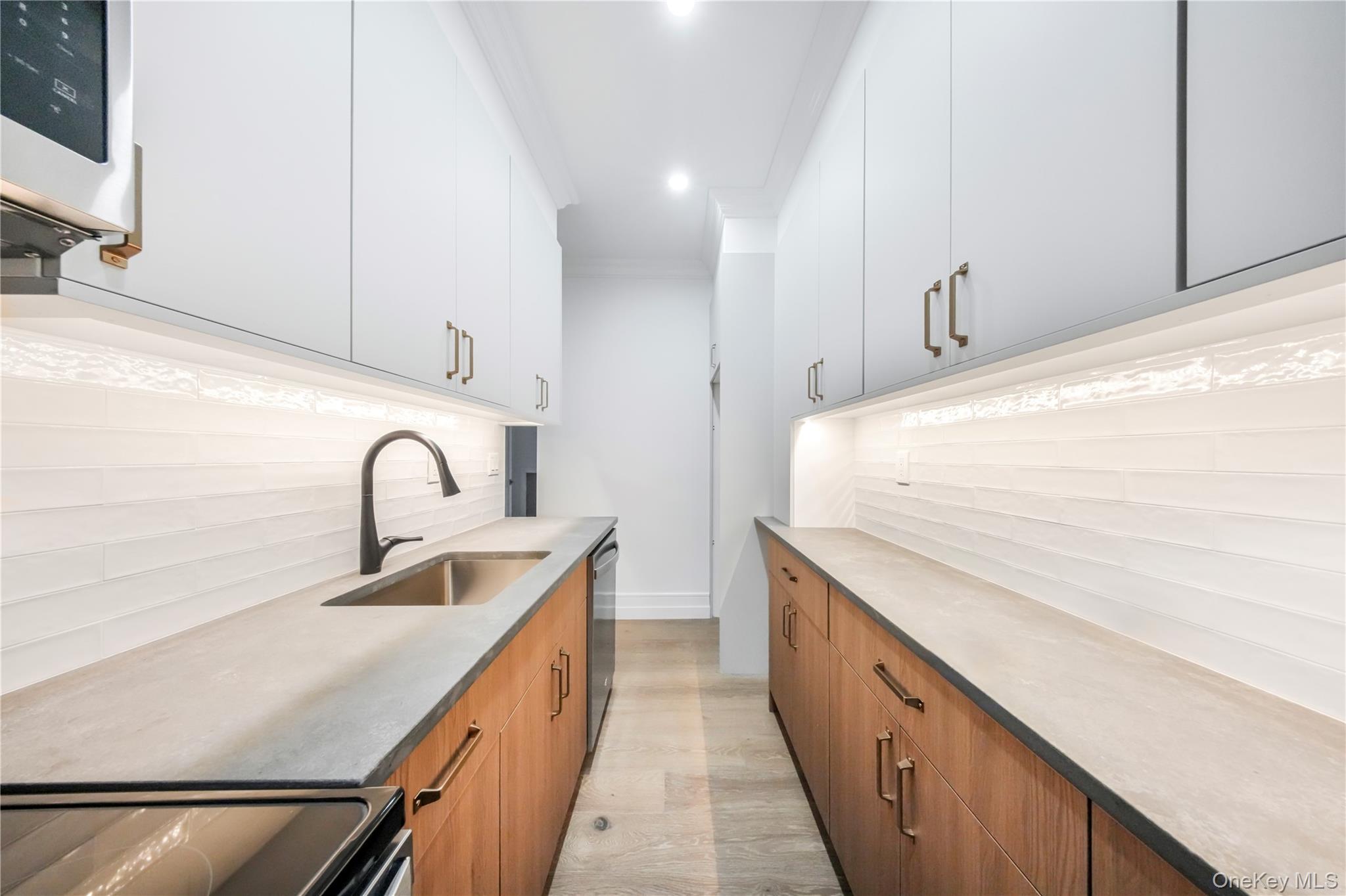 31-14 Crescent Street, Unit 5B Queens, NY 11106 - Photo 12 of 16 Kitchen with appliances with stainless steel finishes, decorative backsplash, light stone counters, brown cabinetry, and recessed lighting